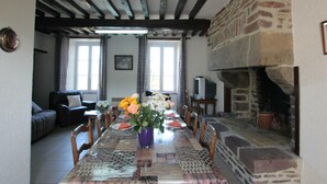 Un comedor con una mesa larga, sillas y un florero. Hay una chimenea de piedra y un televisor sobre una mesa.