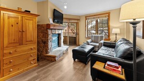 A cozy living room with a fireplace, wooden cabinets, a leather sofa, and a television. - River Run Condo w/ Mountain Views, Overlooks Shared Pool & Hot Tub! (Keystone)