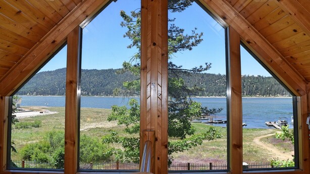 Ein Zimmer mit großen Fenstern und Seeblick, umgeben von Bäumen und Hügeln.