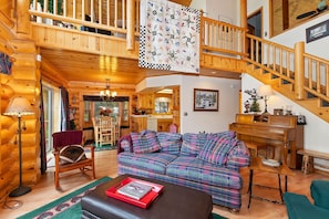 L’intérieur chaleureux d’un chalet en rondins, avec un canapé à carreaux, une table à manger en bois et un escalier menant à l’étage supérieur.