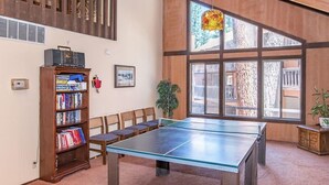 Ein Zimmer mit einem Pingpongtisch, einer Bücherwand, Stühlen und großen Fenstern.