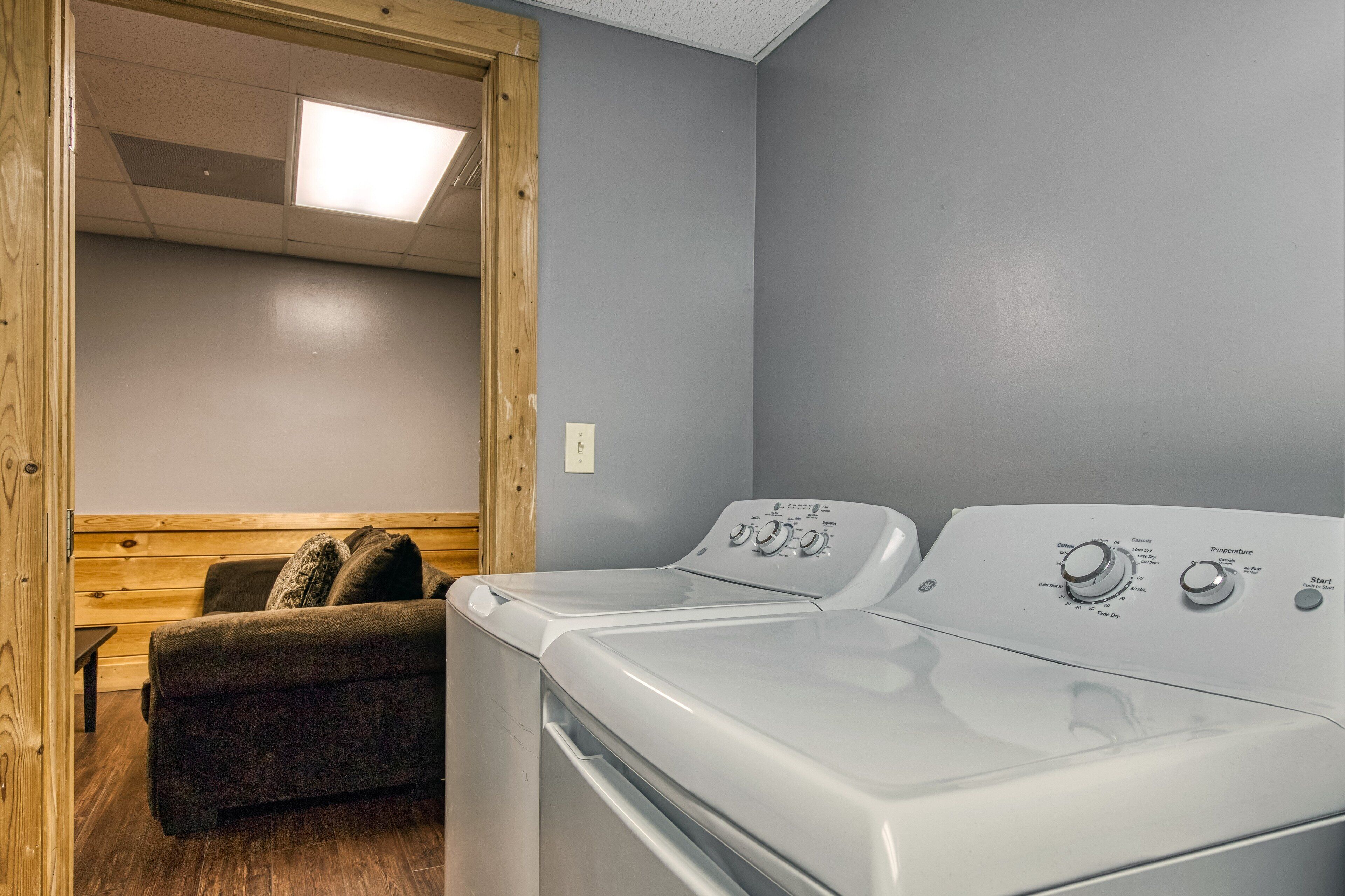 A laundry room with two front-loading washers, a wooden bench, and a ceiling light.