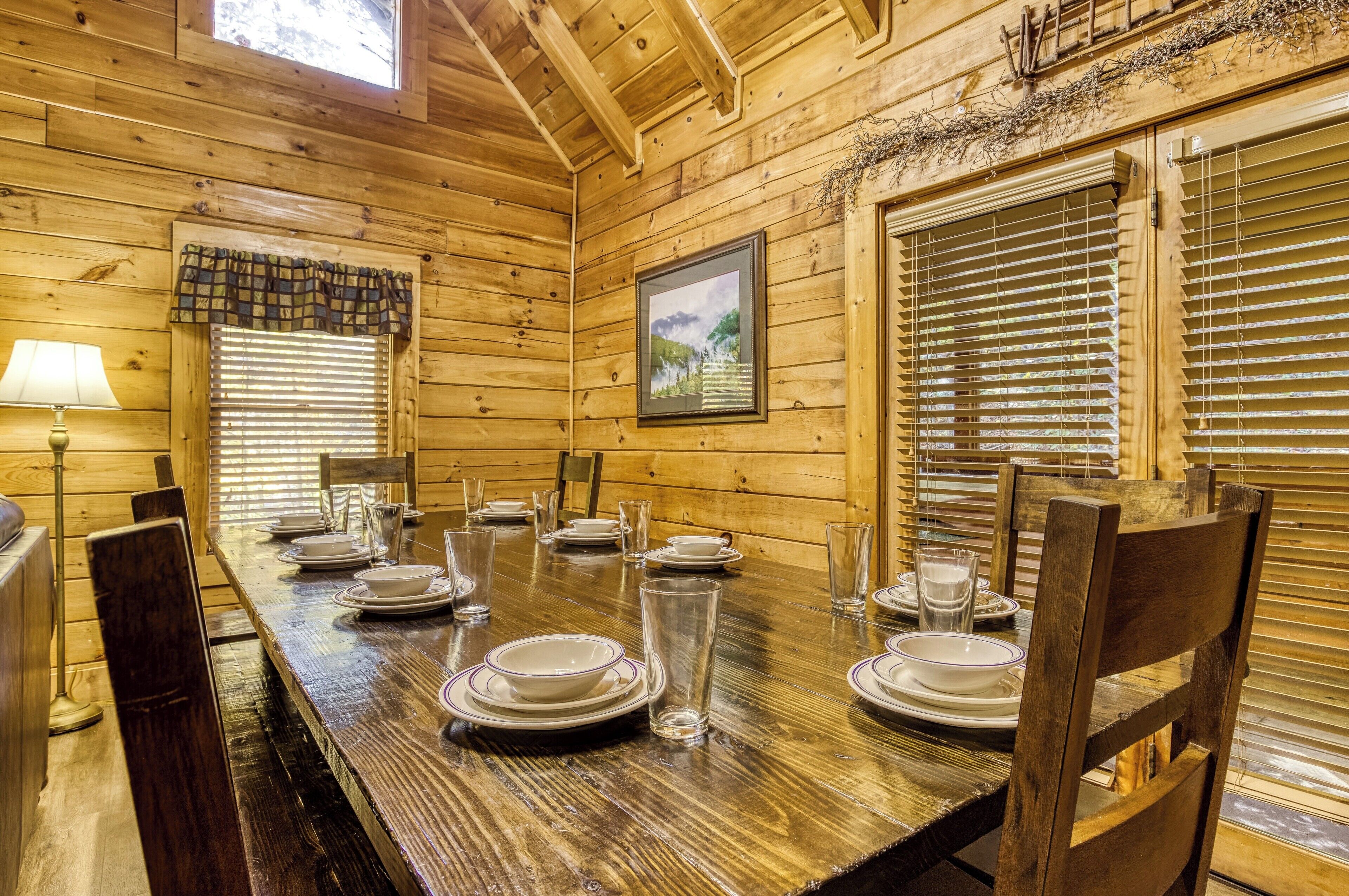 Comedor de madera con una mesa larga dispuesta para cuatro, sillas a cada lado y una ventana con persianas.