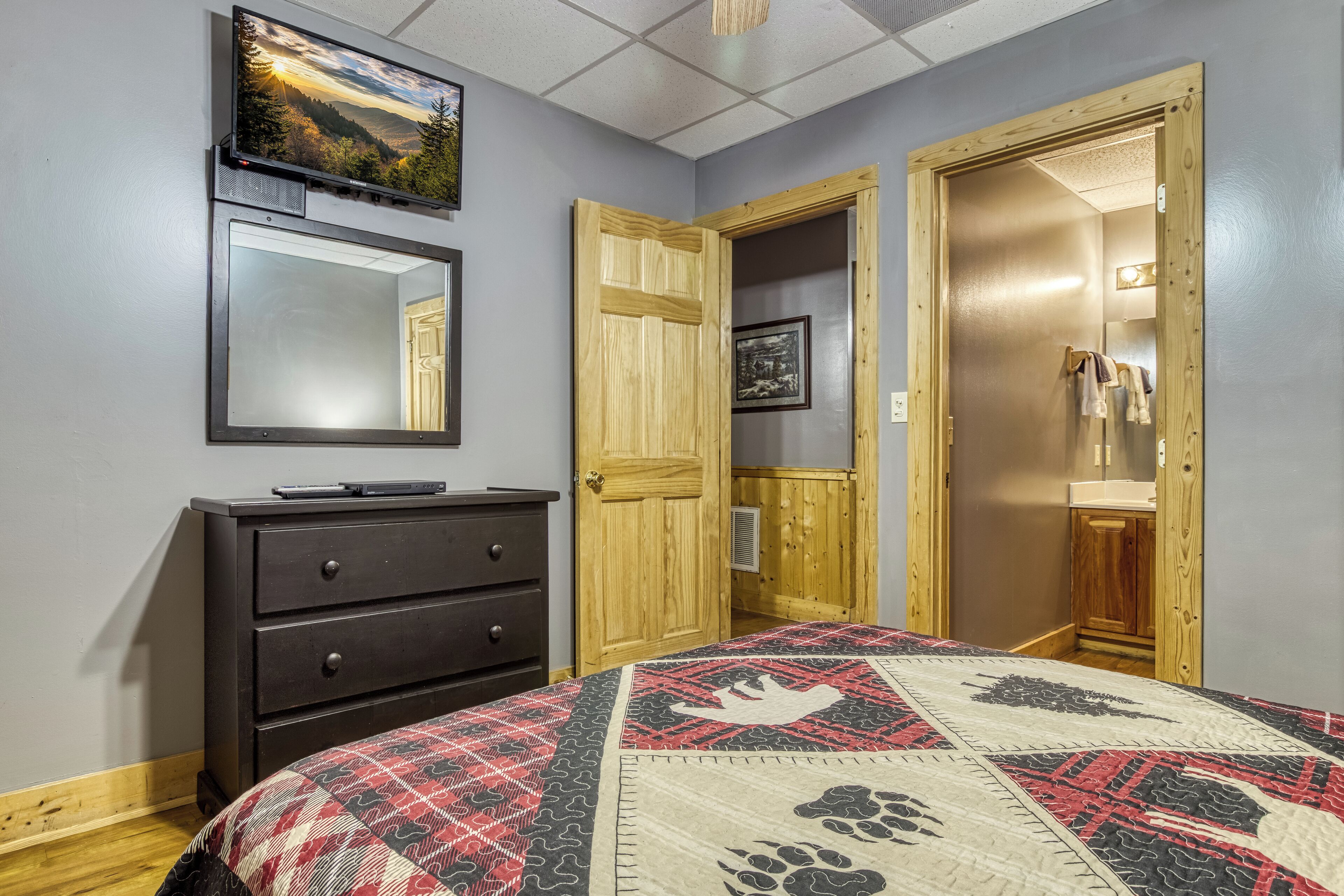 Un dormitorio con cama, cómoda, televisor y puertas de madera.