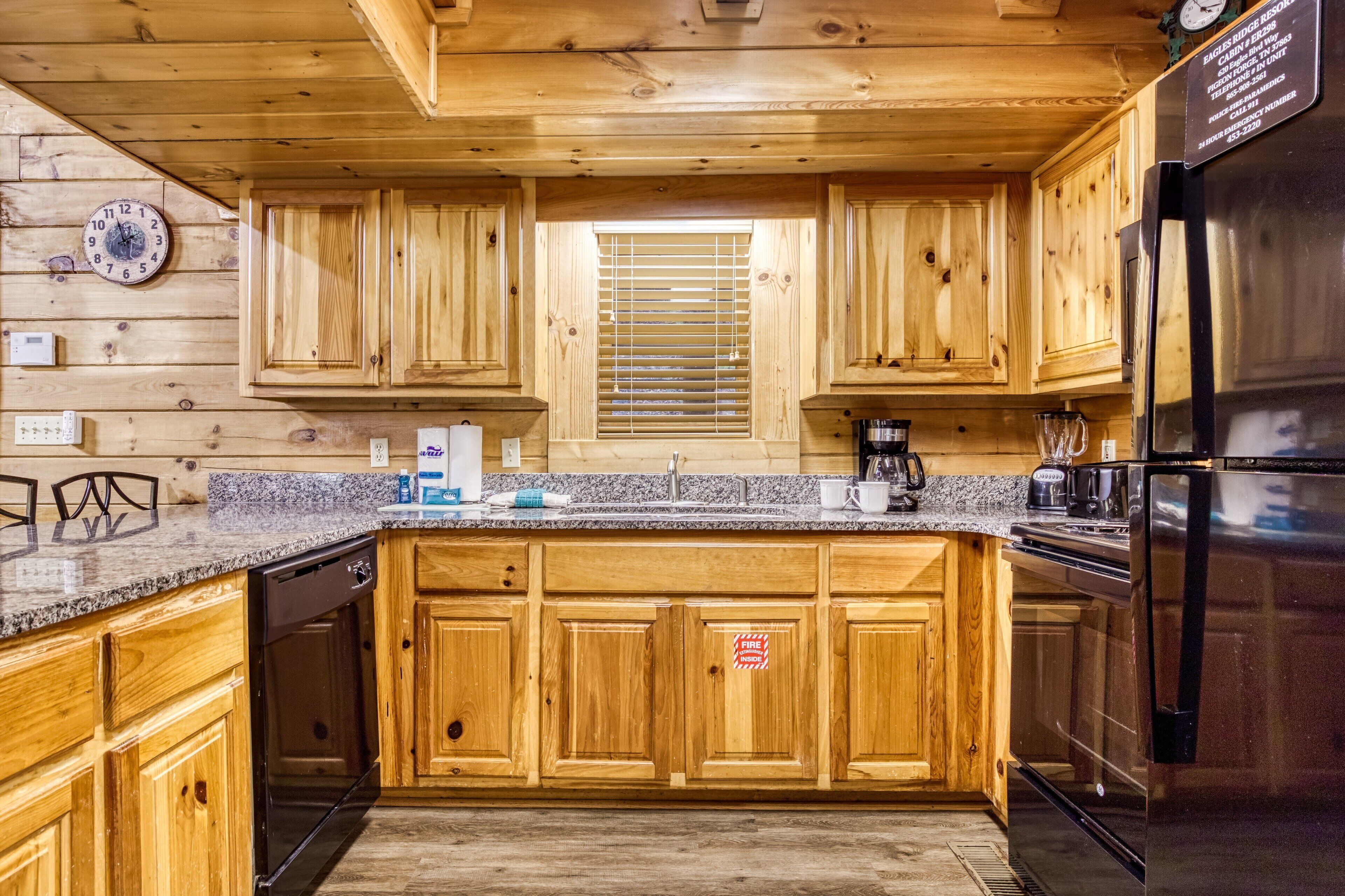 Una cocina tipo cabaña de madera con encimeras de granito, armarios de madera, un refrigerador de acero inoxidable y un reloj en la pared.