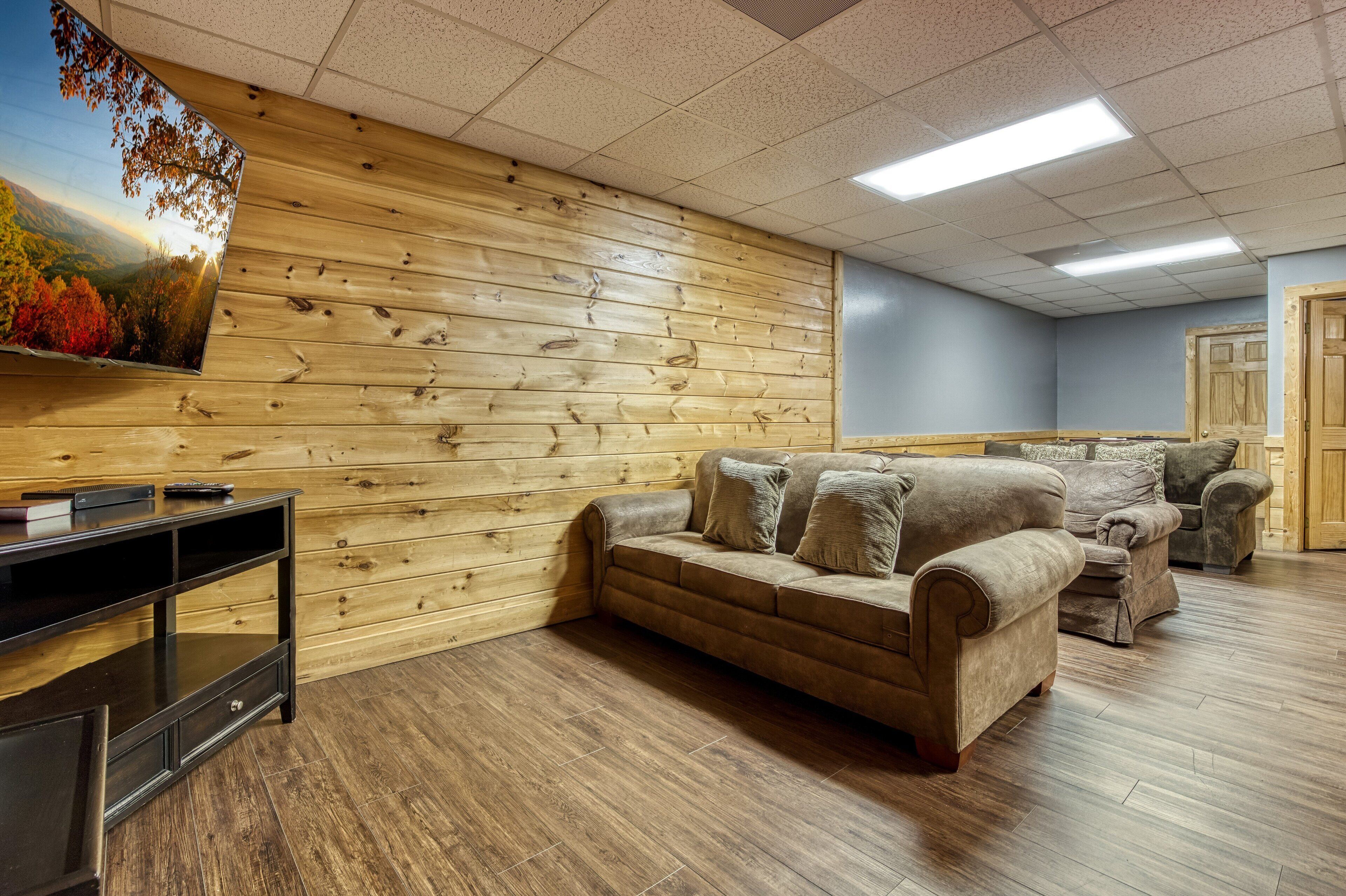 A room with a wooden wall, a brown leather sofa, and a television on a stand.