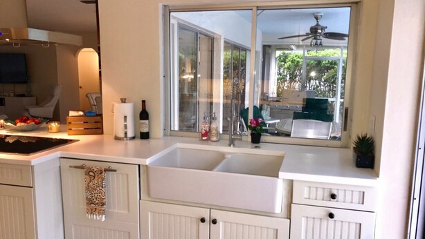 A modern kitchen with white cabinetry, a double sink, and a large window offering a view of the outdoors.