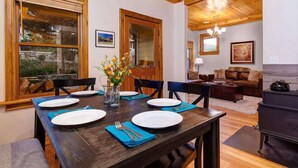 Comedor con una mesa de madera dispuesta para cuatro personas, un jarrón de flores y vistas al exterior a través de amplios ventanales.