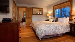 Un dormitorio con cama, cómoda, espejo, ventana con persianas y televisor en la pared.