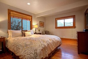 Une chambre à coucher avec un grand lit, des cadres de fenêtre en bois, une table de chevet et une commode.