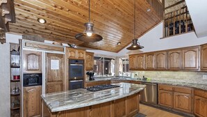 A spacious kitchen with wooden cabinetry, a central island, and a large window providing natural light. - Running Bear by Destination Big Bear : Walk to Snow Summit! Pool Table!Great Backyard w/ Hot Tub! Master Suite! (Big Bear Lake)