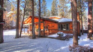 A cabin with a covered porch, large windows, and a snow-covered landscape. - Running Bear by Destination Big Bear : Walk to Snow Summit! Pool Table!Great Backyard w/ Hot Tub! Master Suite! (Big Bear Lake)