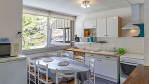 Een compacte keuken met witte kastjes, een eettafel met vier stoelen, een raam met uitzicht op groen, en een inbouwoven.