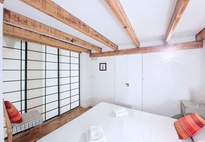 A room with a bed, a window with a grid pattern, wooden beams, and a small table.