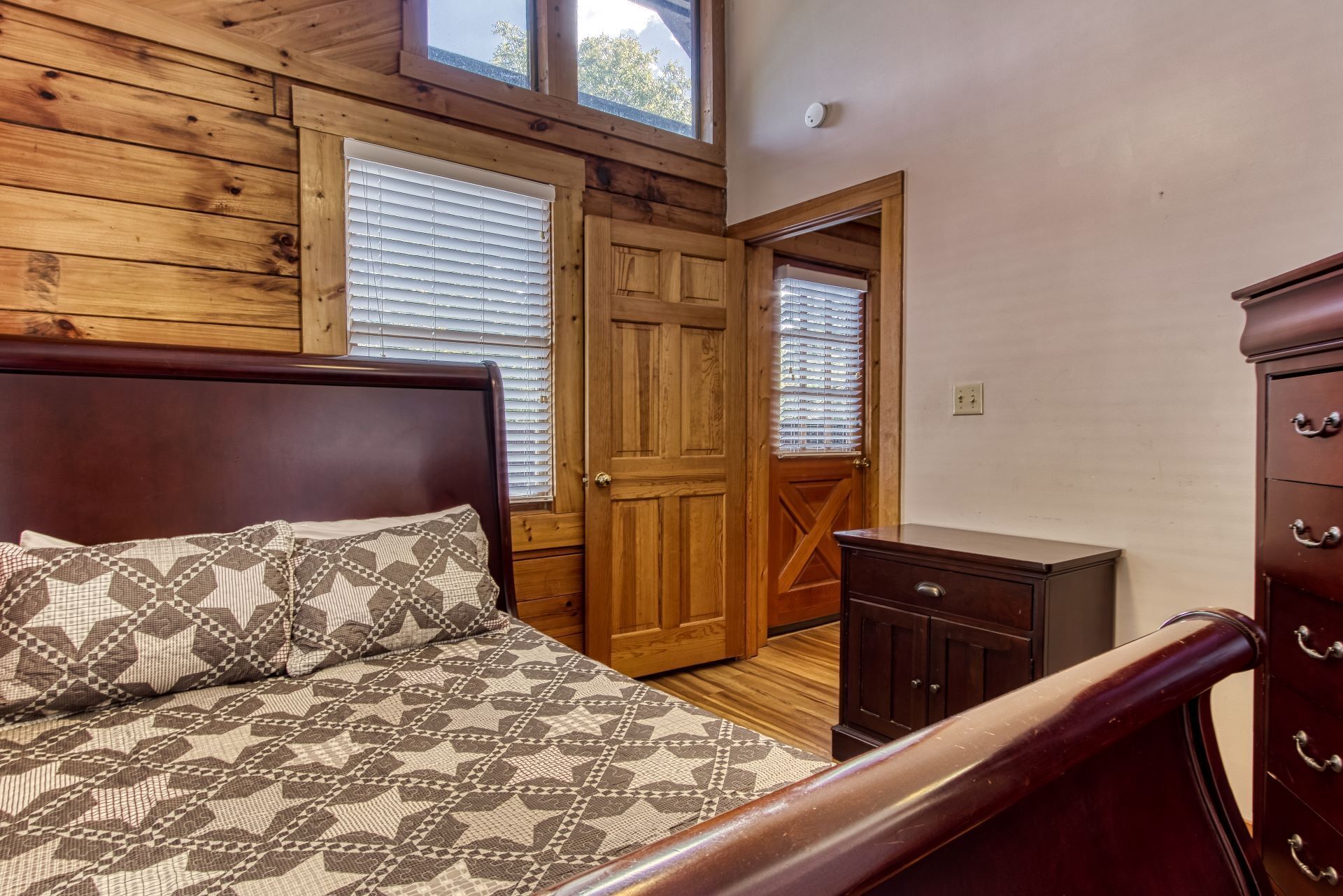 Un dormitorio con cabecera de madera, colcha estampada, cómoda y puerta que da a otra habitación.