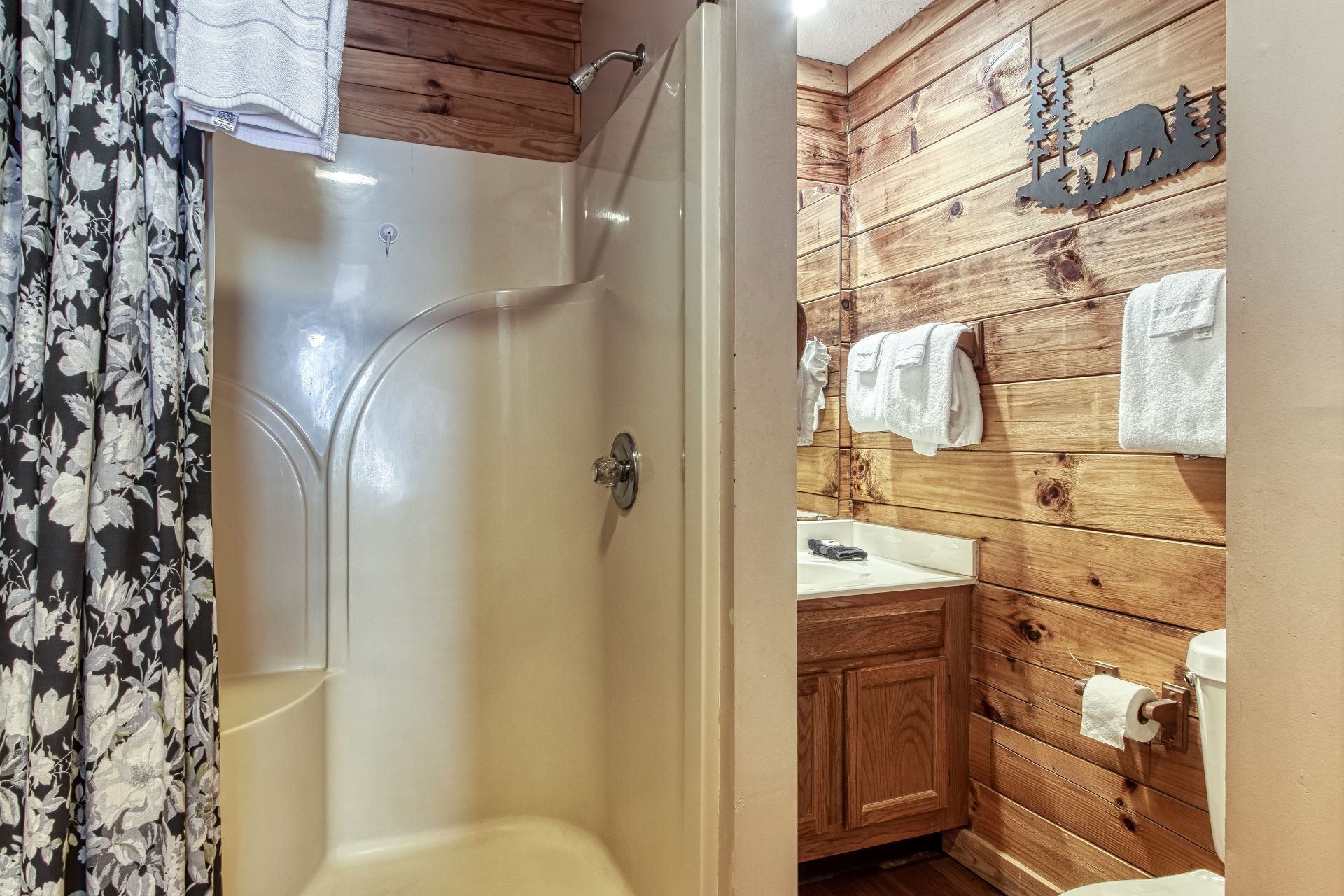 Ein Badezimmer mit Dusche, Holzvertäfelung und Waschbecken. Ein Handtuch hängt an der Wand.