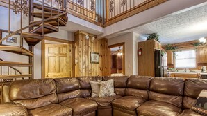 Ein geräumiger Wohnbereich mit einem großen Ledersofa, einer Holztreppe und einer Küchenzeile mit Holzschränken und einem Kühlschrank.
