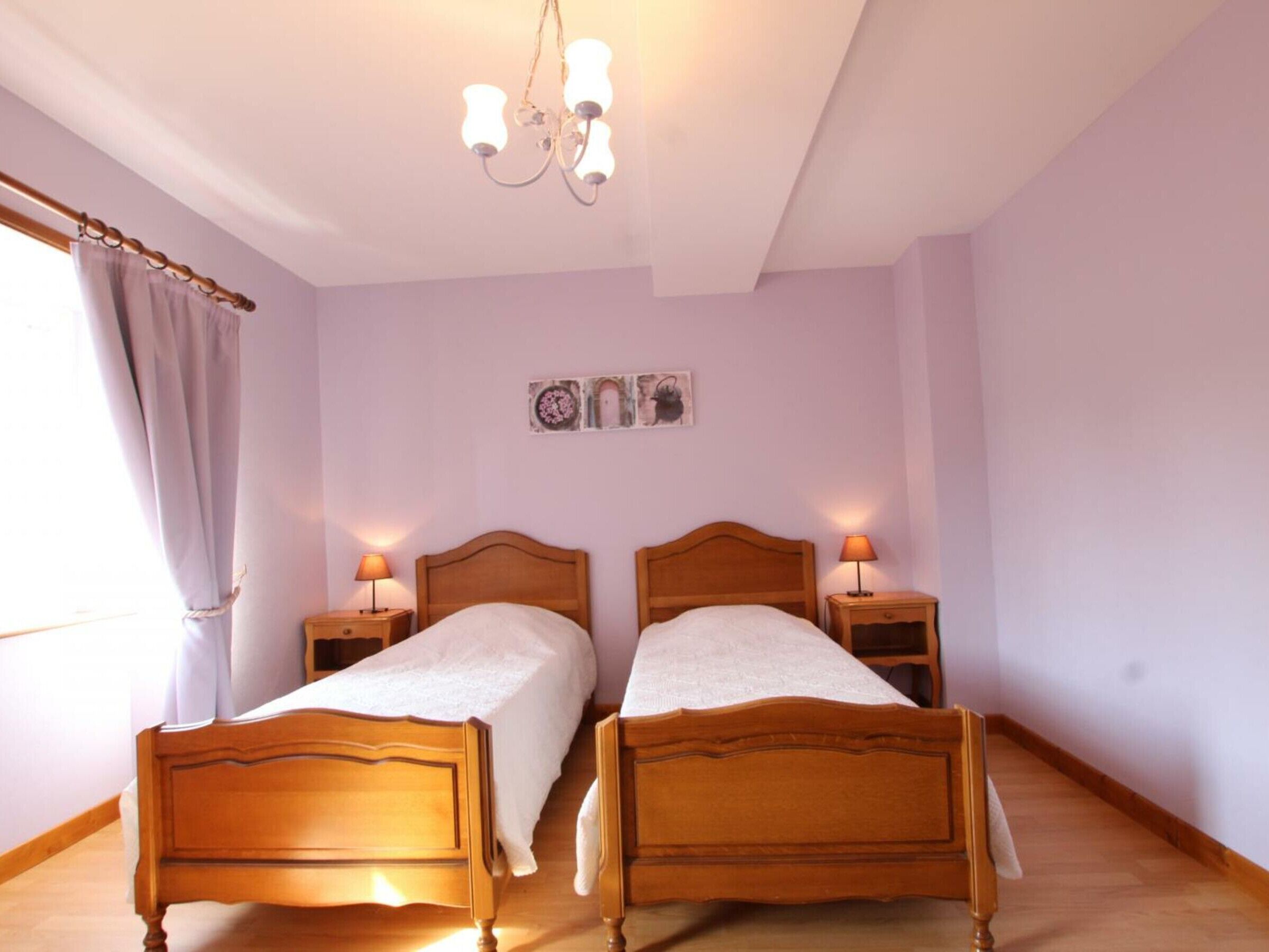A bedroom with two wooden beds, a chandelier, and a window with curtains.