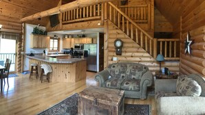 A log cabin interior with a kitchen, dining area, and a staircase leading to an upper level. - The Driftless Escape! Modern, large cabin/57 private acres in WI drift less area (Richland Center)