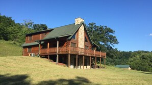 A log cabin with a stone chimney, a balcony, and a grassy hill in the background. - The Driftless Escape! Modern, large cabin/57 private acres in WI drift less area (Richland Center)