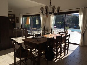 Zona pranzo con tavolo e sedie in legno, un lampadario e vista su un patio esterno con piscina.