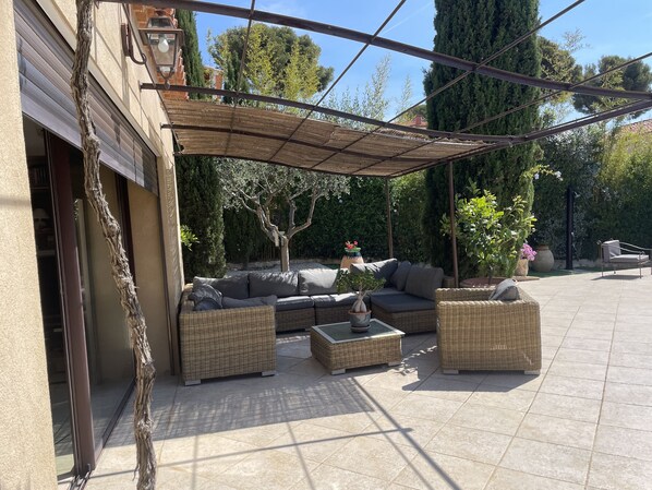 An outdoor patio with wicker furniture, a pergola, and a view of the surrounding garden.