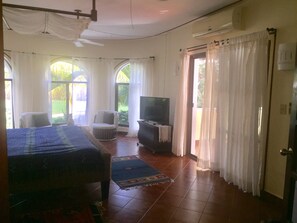 Un dormitorio con una cama, televisor, sillón y ventana.