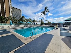 Relax by the resort pool surrounded by palm trees and lounge chairs.