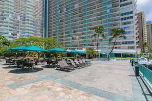 Relax in a shaded outdoor seating area surrounded by palm trees and a high-rise building with balconies.