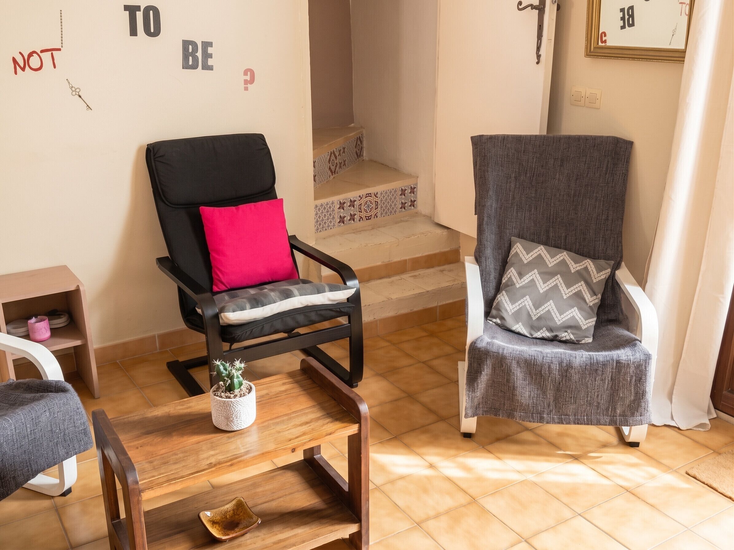 Een kamer met twee fauteuils, een tafeltje, een plant in pot en een trap.