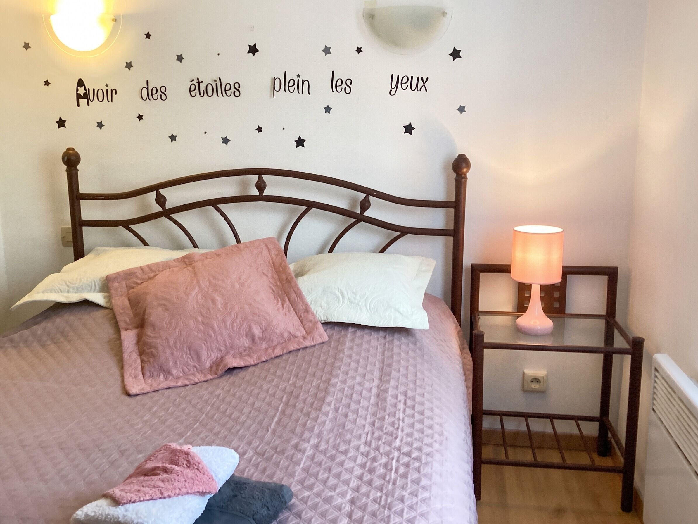 A neatly made bed with pillows, a bedside lamp, and a wall with star decorations and French text.