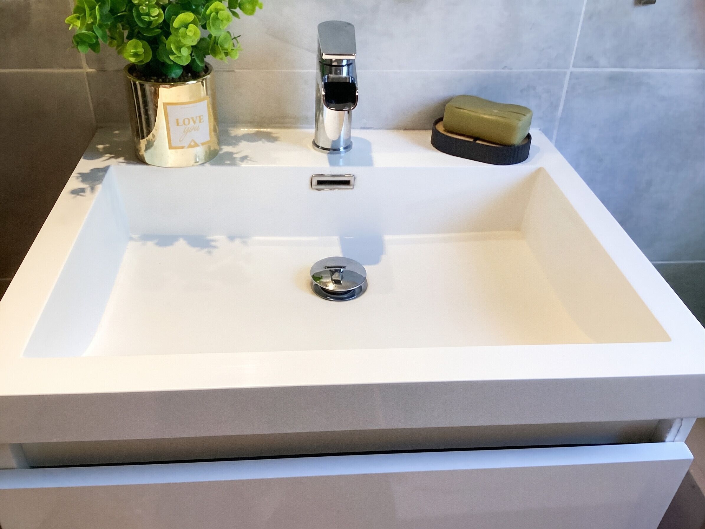 Un lavabo blanc pour la salle de bain, doté d’un robinet moderne, d’une petite plante en pot et d’un porte-savon.
