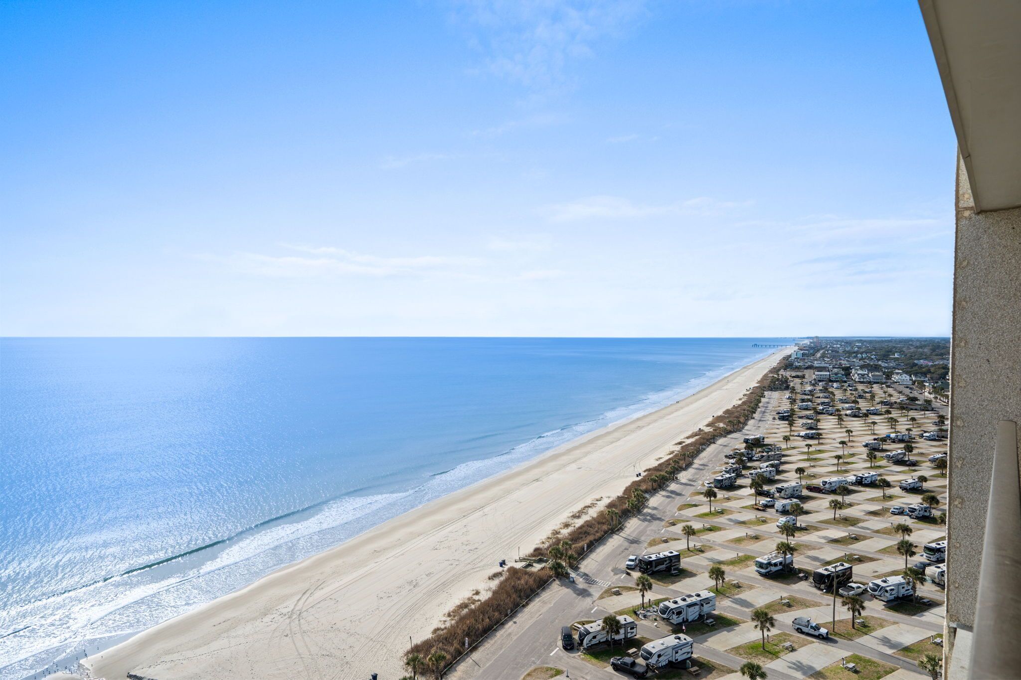 A beachside parking lot with RVs, a sandy beach, and the ocean.