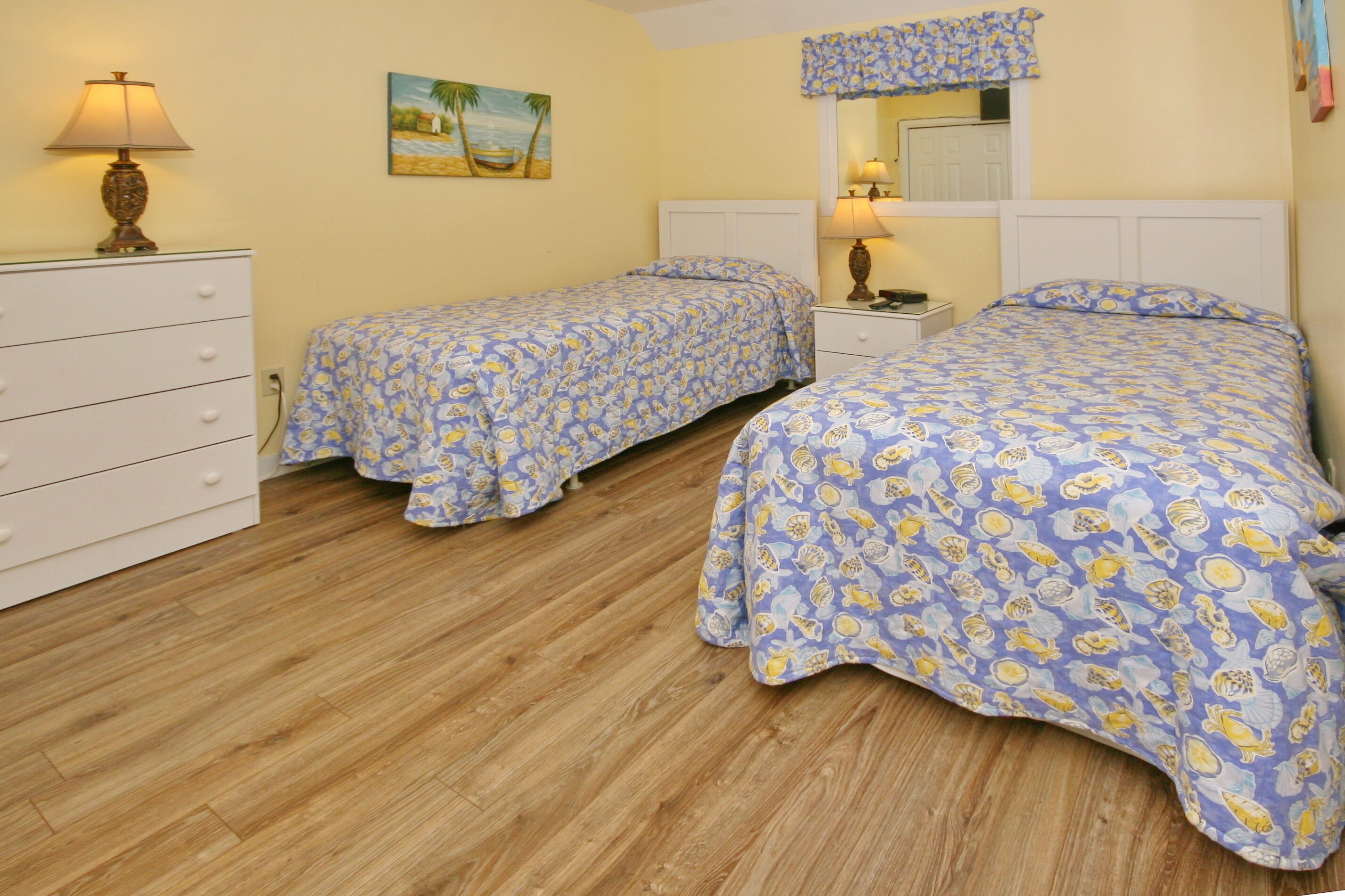 A bedroom with two beds, a dresser, a nightstand, a lamp, and a painting on the wall.