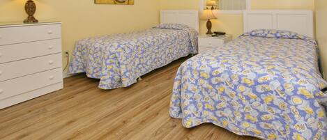 A bedroom with two beds, a dresser, a nightstand, a lamp, and a painting on the wall.