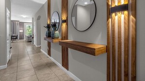 A hallway with a wooden shelf, a round mirror, and a wall-mounted light fixture. - 6 Bedrooms / 5 Bathrooms / Paradise Palms (8956 SP) (Kissimmee)