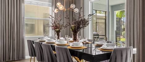 A dining area with a glass table, grey chairs, and a modern chandelier.