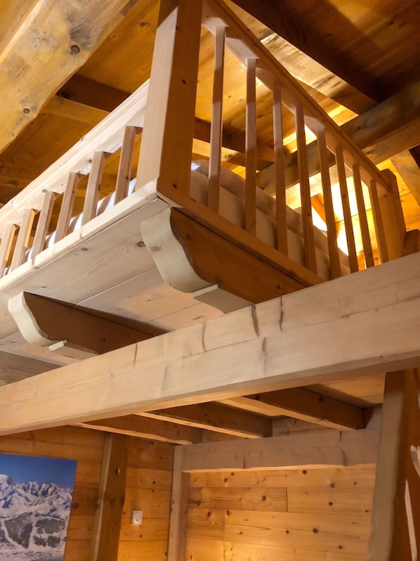 A wooden balcony structure with railings, supported by beams, and a view of a mountain landscape.