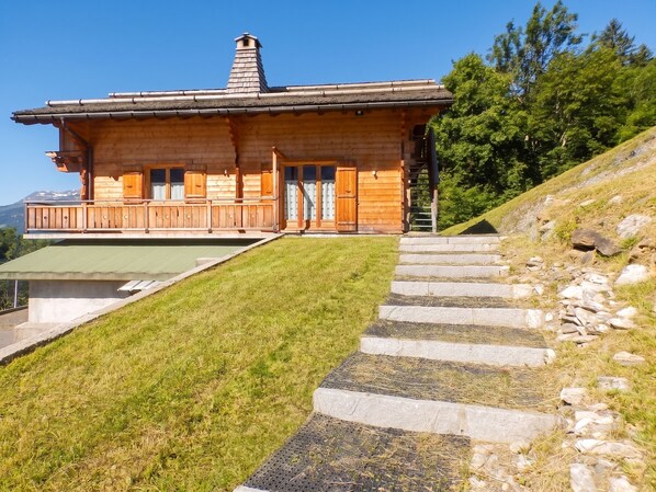 A wooden cabin with a balcony, a chimney, and a stone staircase leading up to the entrance.
