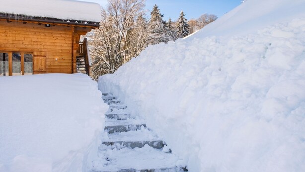 A wooden cabin with a snow-covered roof and steps leading up to it.