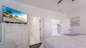 A bedroom with a bed, a dresser, a television displaying a beach scene, and a hallway leading to other rooms. - Lake View! Amazing Sunsets w/West Facing Pool (Clermont)