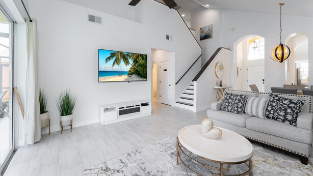 A spacious living room with a ceiling fan, a flat-screen TV, a staircase, and a dining area. - Lake View! Amazing Sunsets w/West Facing Pool (Clermont)