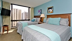 Een hotelkamer met twee bedden, een televisie, een raam met uitzicht over de stad en kunst aan de muur.