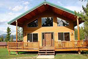 Une cabane en rondins à deux étages, dotée d’une véranda, de grandes fenêtres et d’un toit végétalisé.
