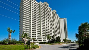 Ein hohes, mehrstöckiges Hotel mit einheitlicher Fassade, umgeben von Grün und blauem Himmel.