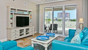 Ein Wohnzimmer mit Fernseher, einer weißen Unterhaltungsanlage, einem blauen Sofa und einem Balkon mit Blick auf Gebäude.