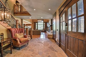 A spacious hallway with a stone floor, a leather armchair, a wooden staircase, and a large wooden door.