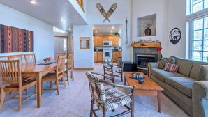 Uma sala de estar ampla com uma mesa de jantar de madeira, cadeiras, um sofá e uma lareira.