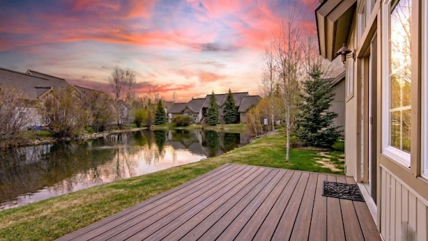Um deck de madeira com vista para um lago calmo e casas ao fundo.