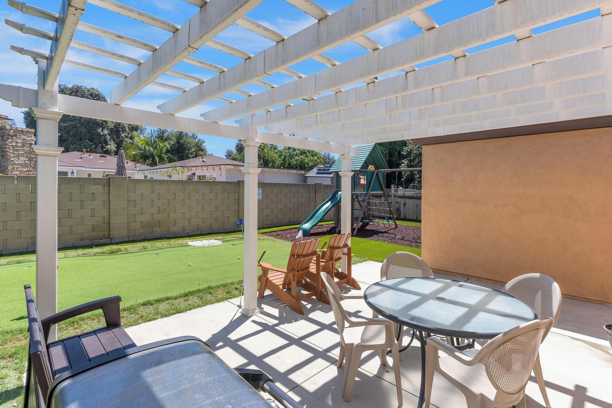 A covered patio area with a table and chairs, a slide, and a brick wall in the background.